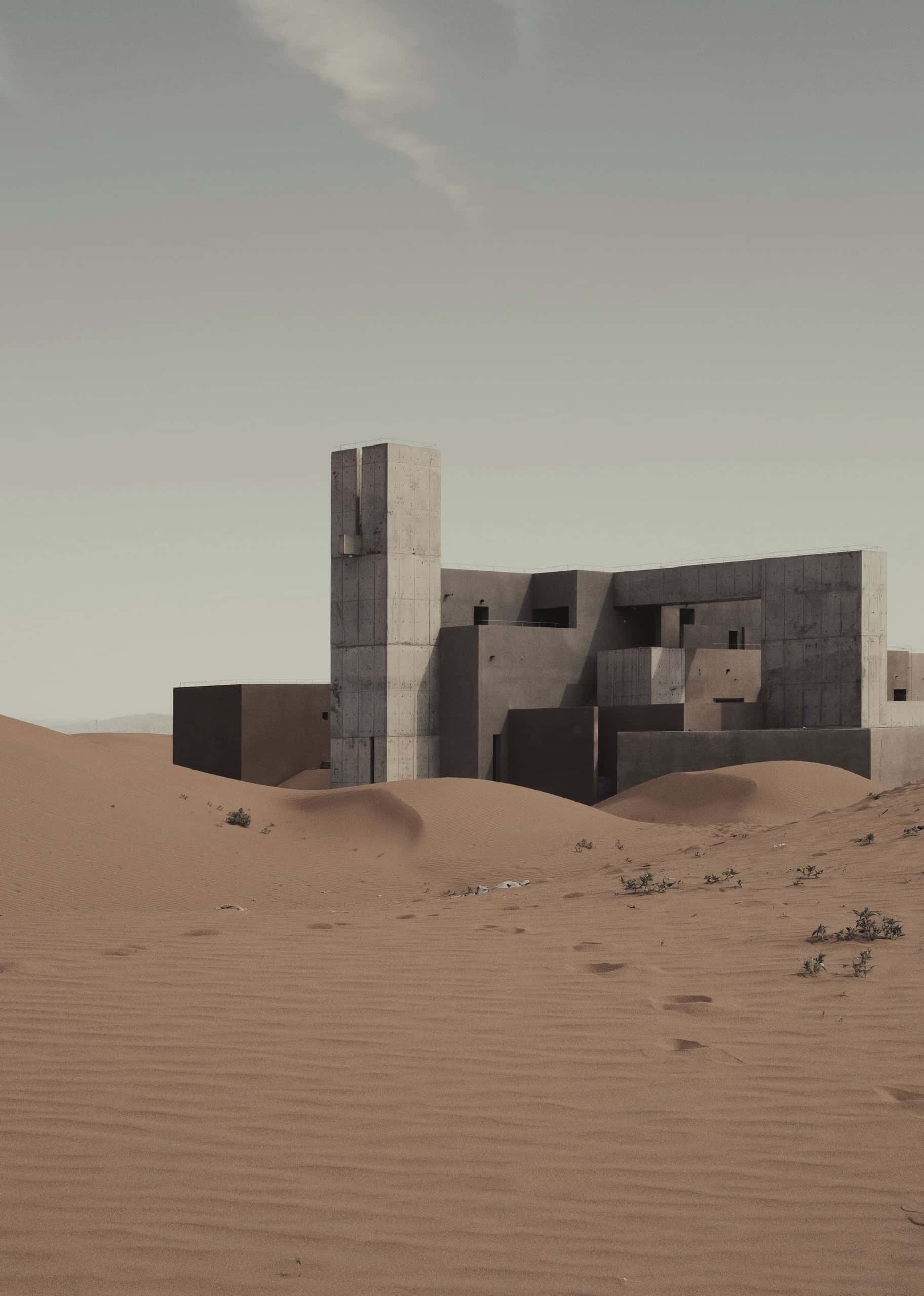 A cluster of earth-coloured volumes and a single tower half-buried in desert sand.