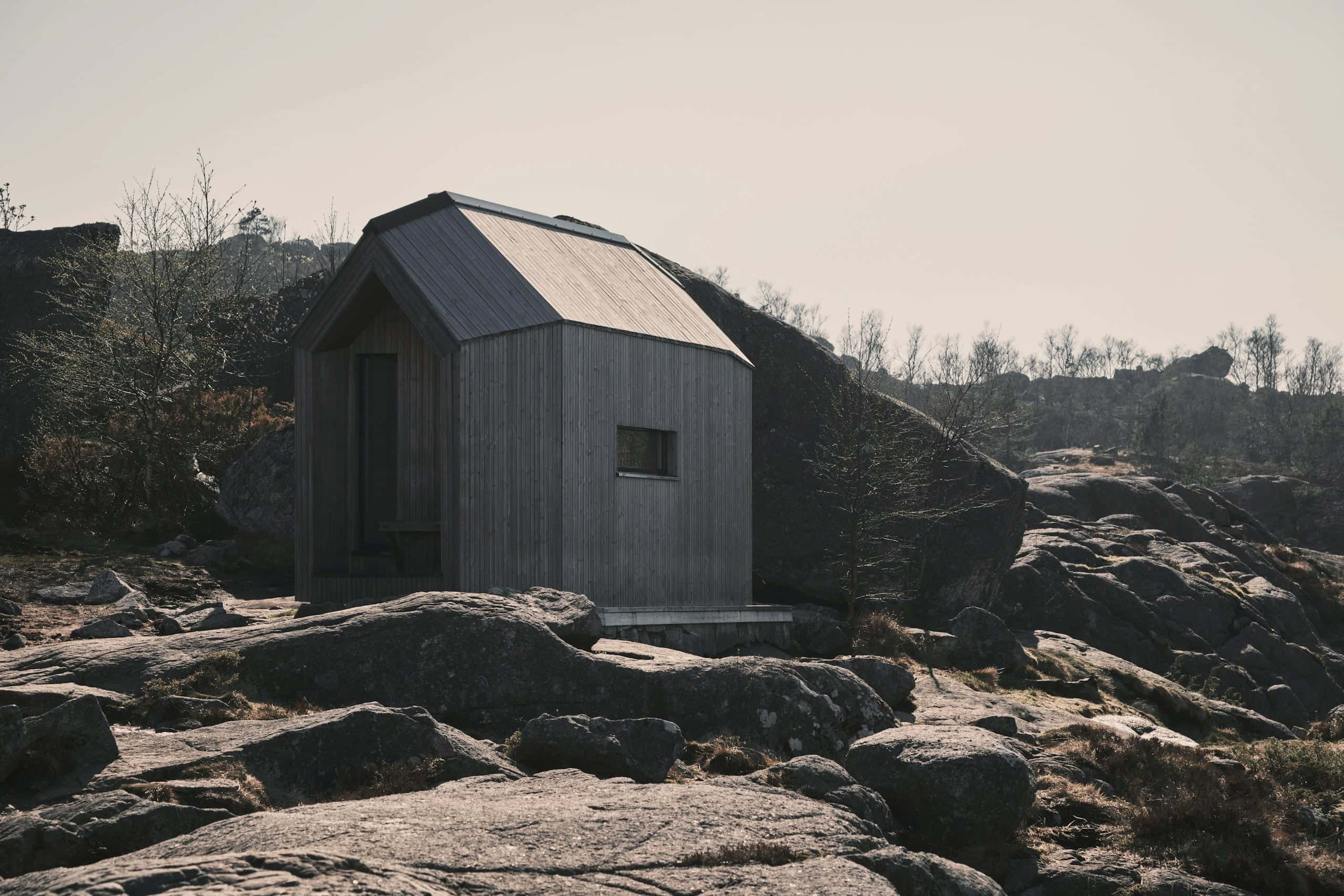 A small pitched-roof refuge clad in weathered grey among granite boulders.