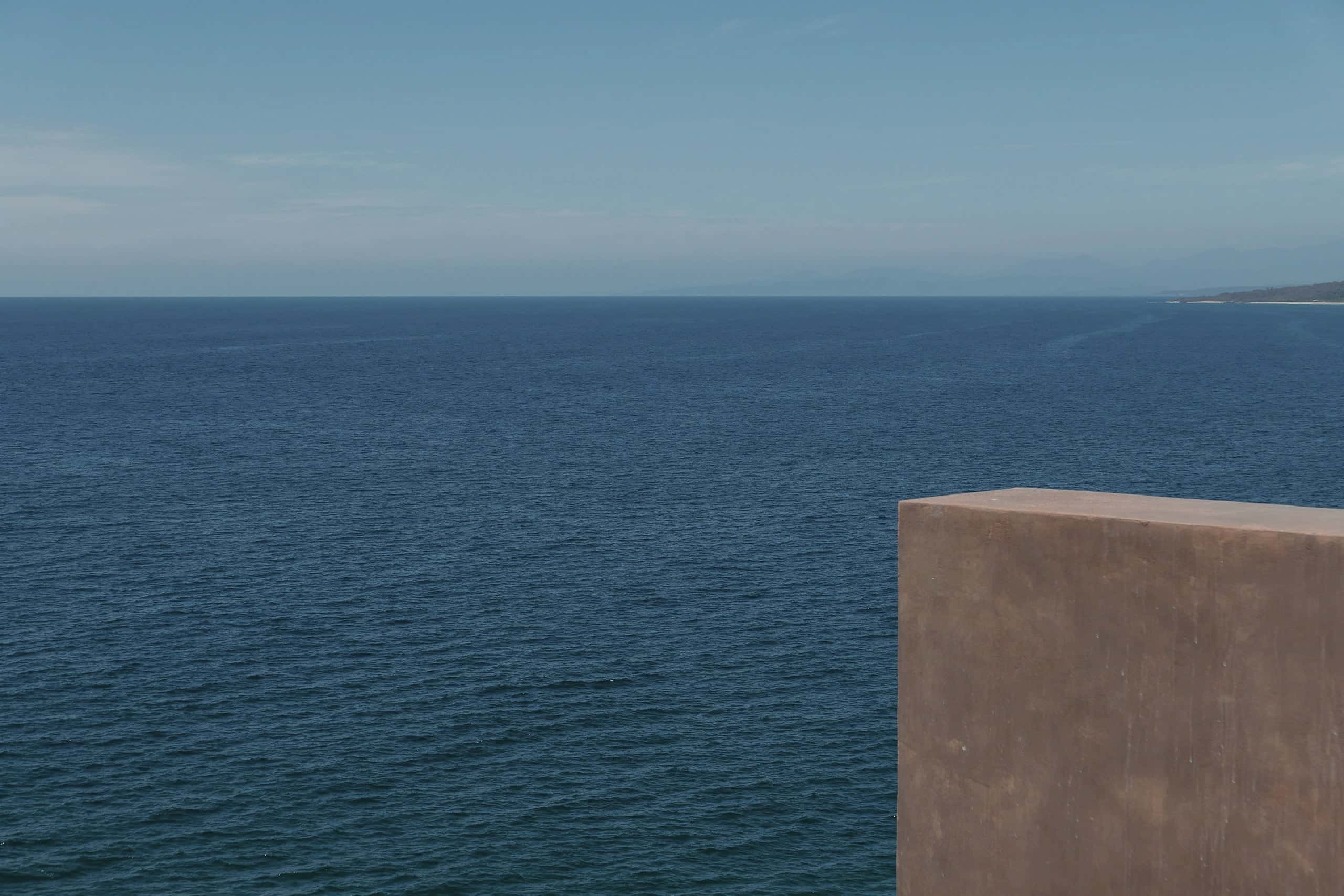 A red pigmented concrete parapet at the edge of a calm, deep-blue sea.