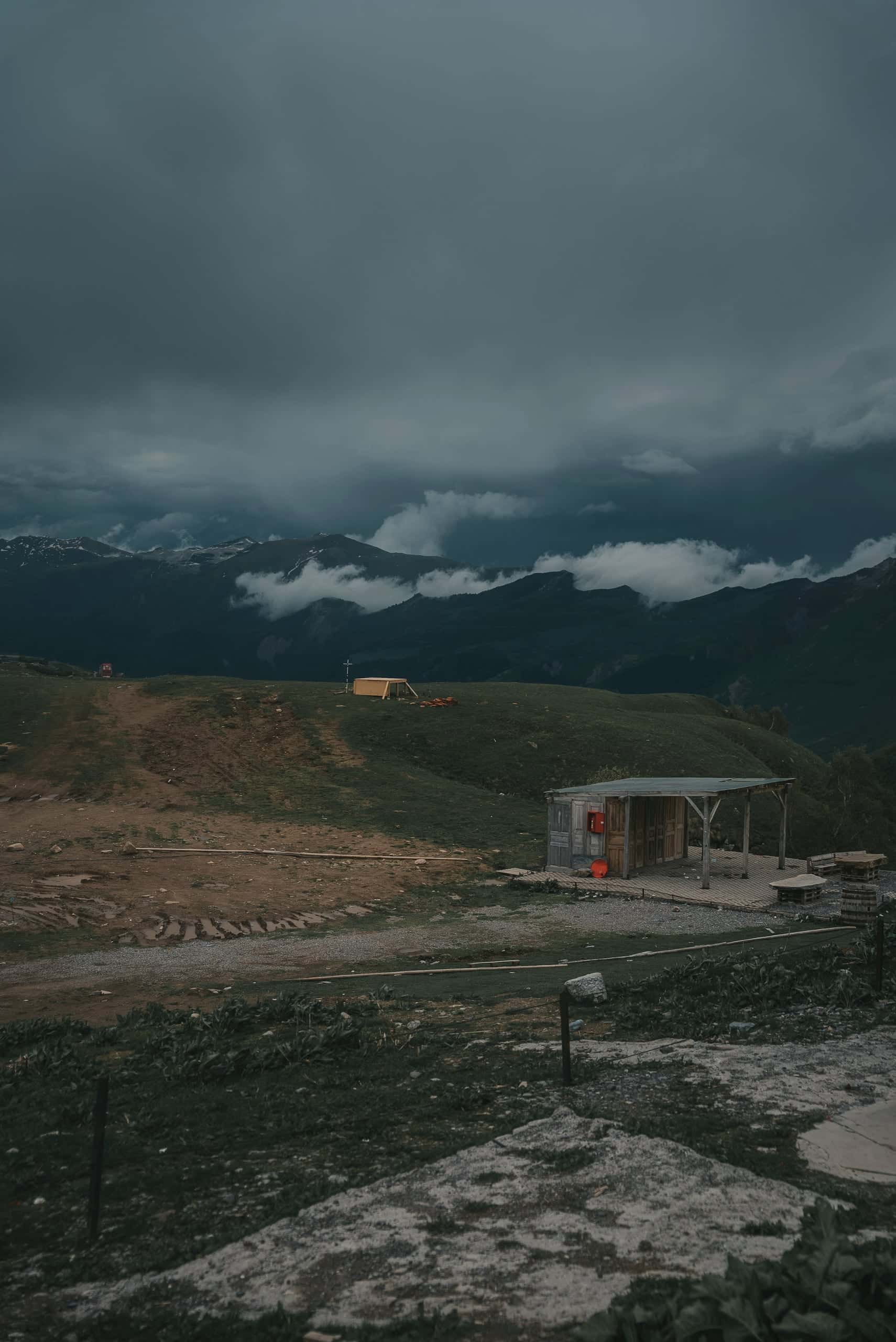 Low cloud over a mountain valley, a small building on the open slope below.