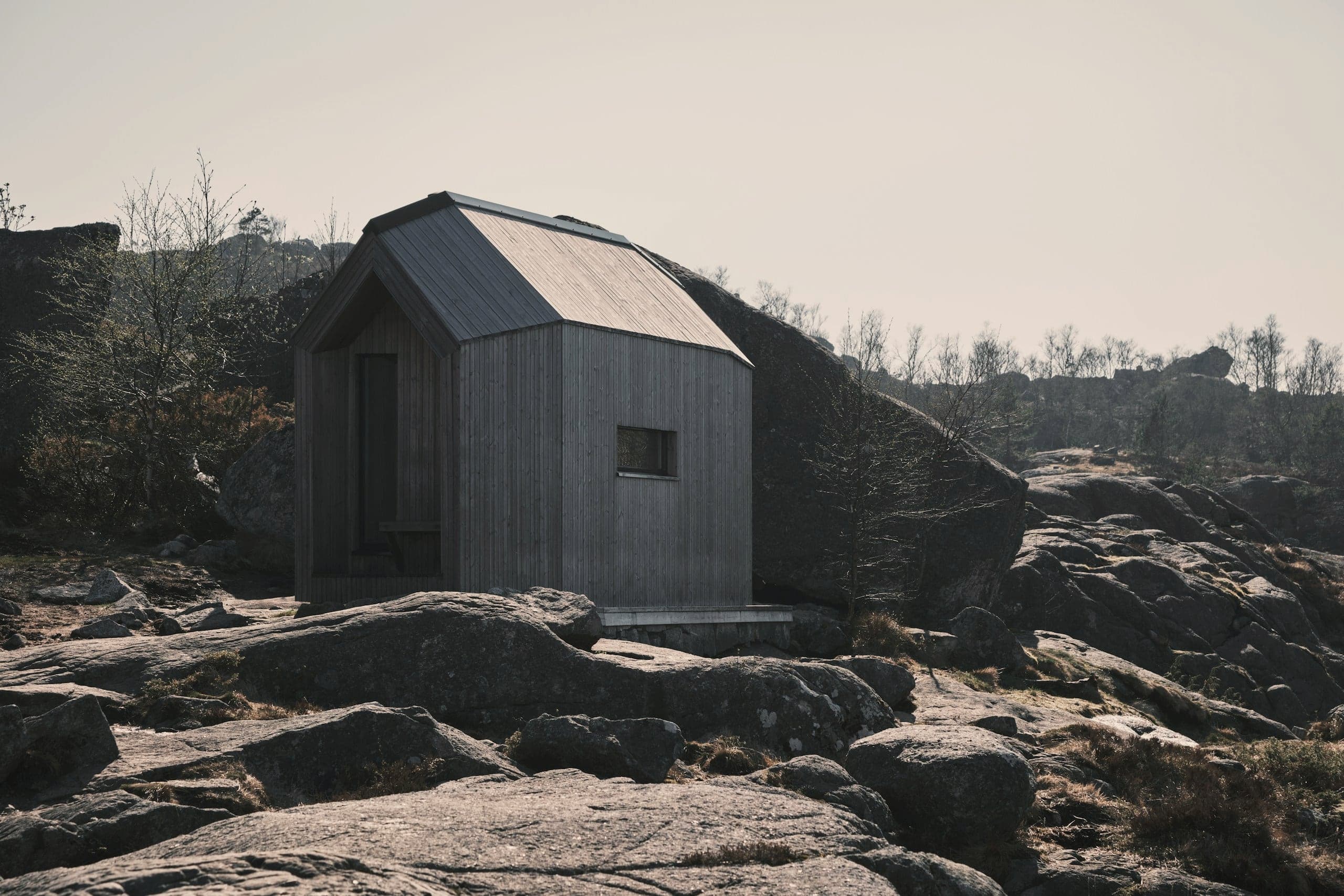 A small pitched-roof refuge clad in weathered grey among granite boulders.