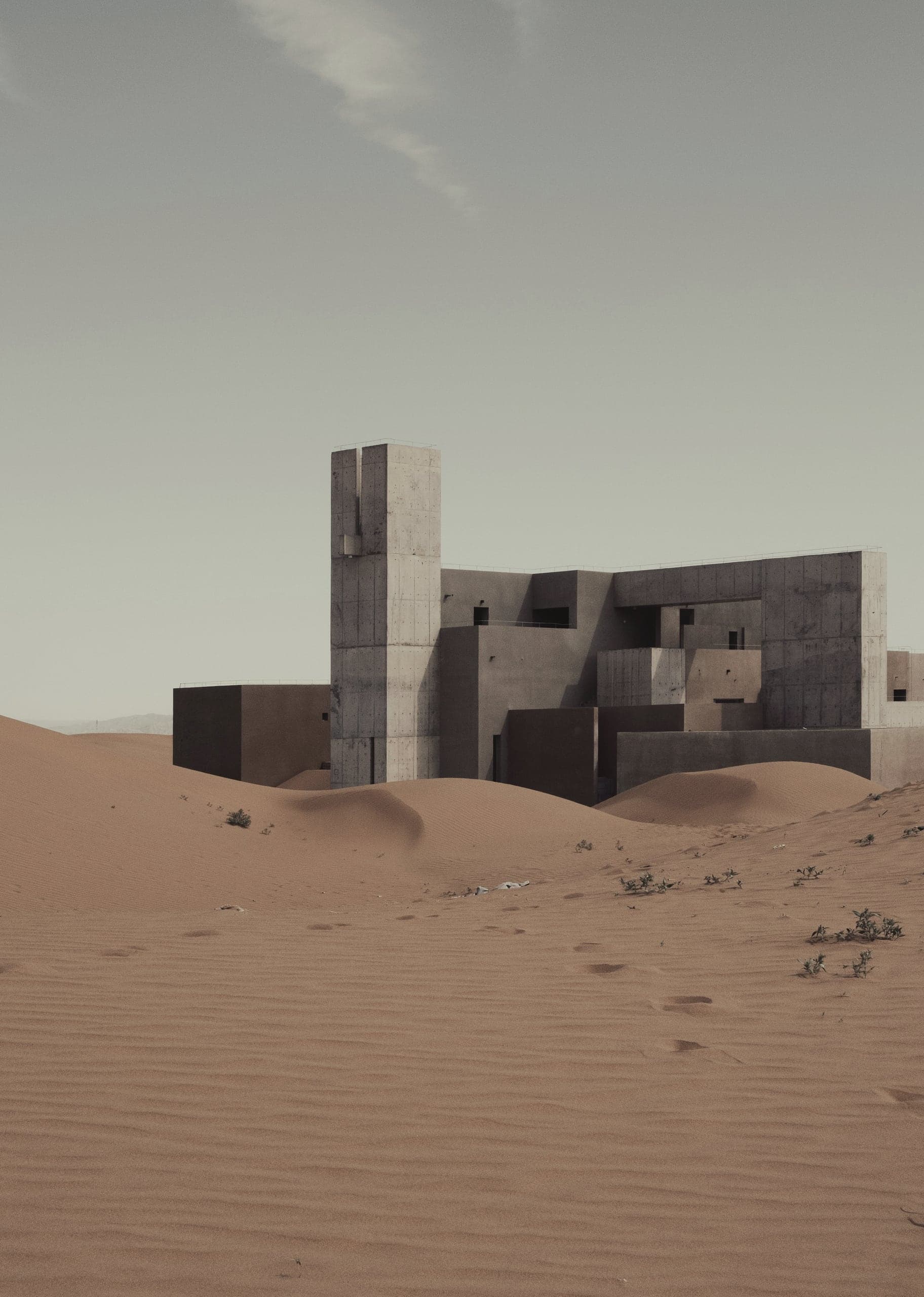 A cluster of earth-coloured volumes and a single tower half-buried in desert sand.