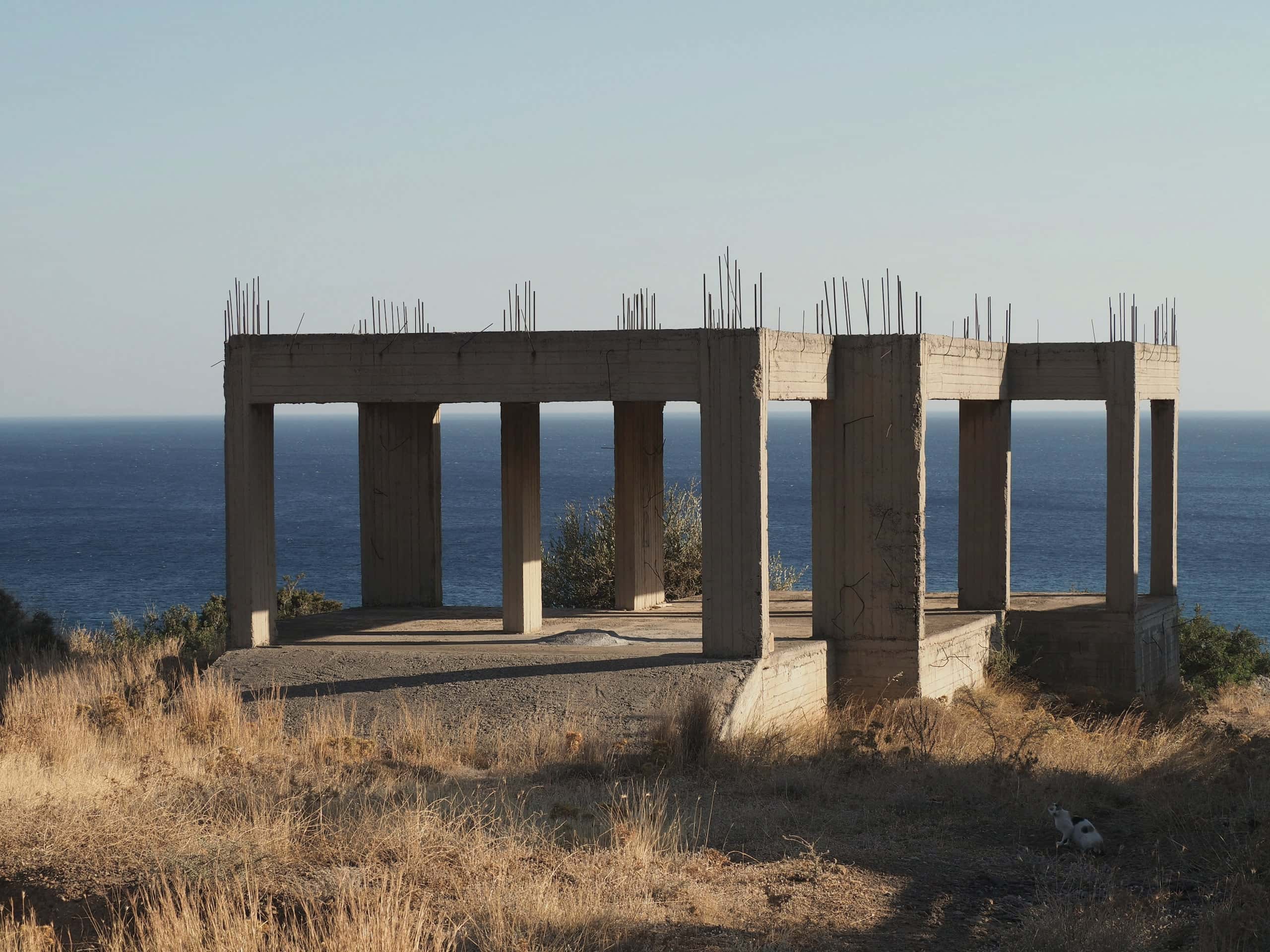 The concrete frame of the house under construction on a dry headland above the sea.