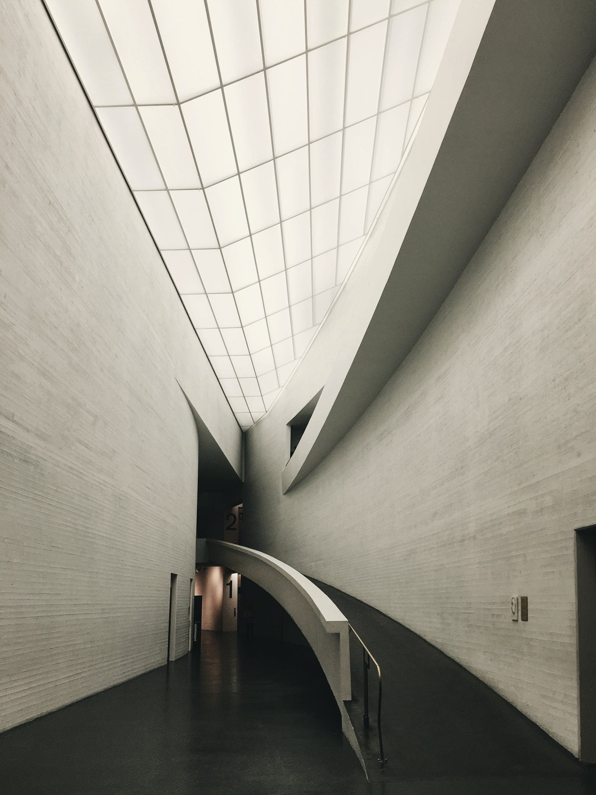 A narrow top-lit passage between white walls, a bridge crossing over dark water.