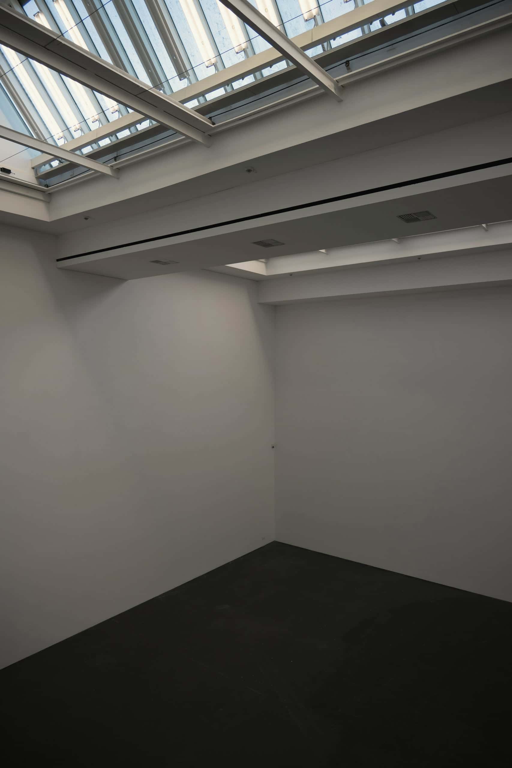 A tall white room lit by a rooflight above a dark floor.