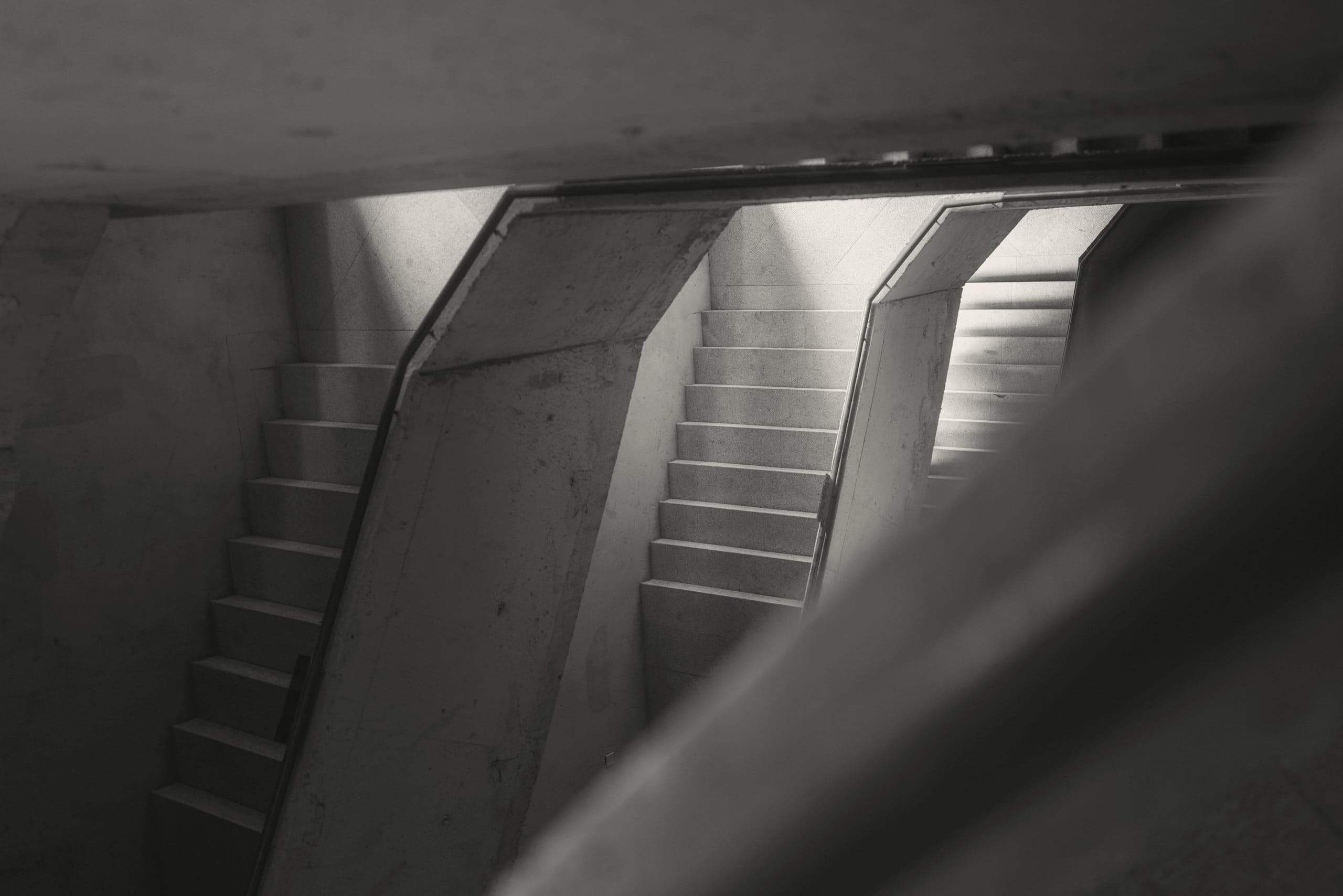 Concrete stairs rising in parallel through a dark shaft, lit from above.