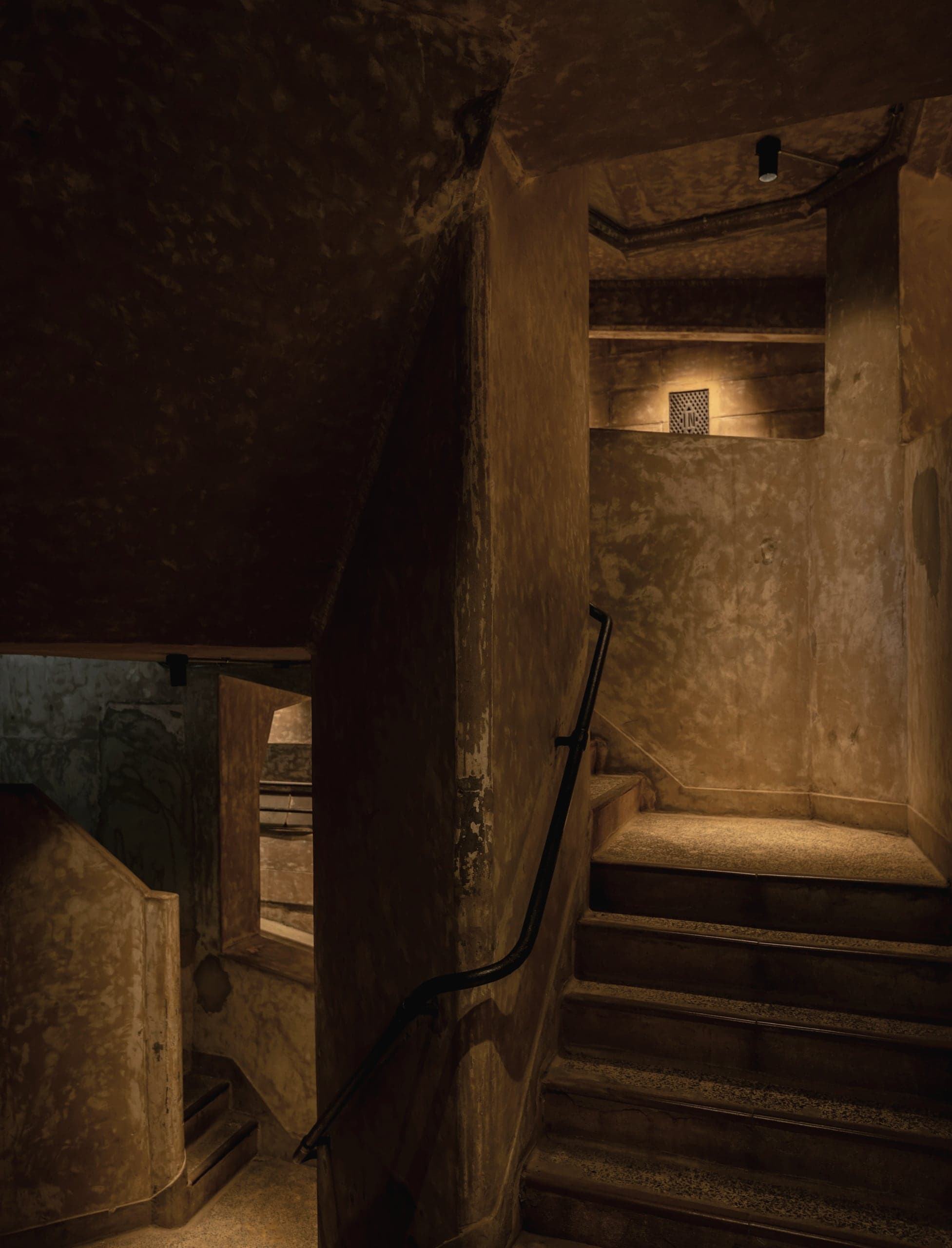A narrow stone stair lit warm at the top of a dark stairwell.