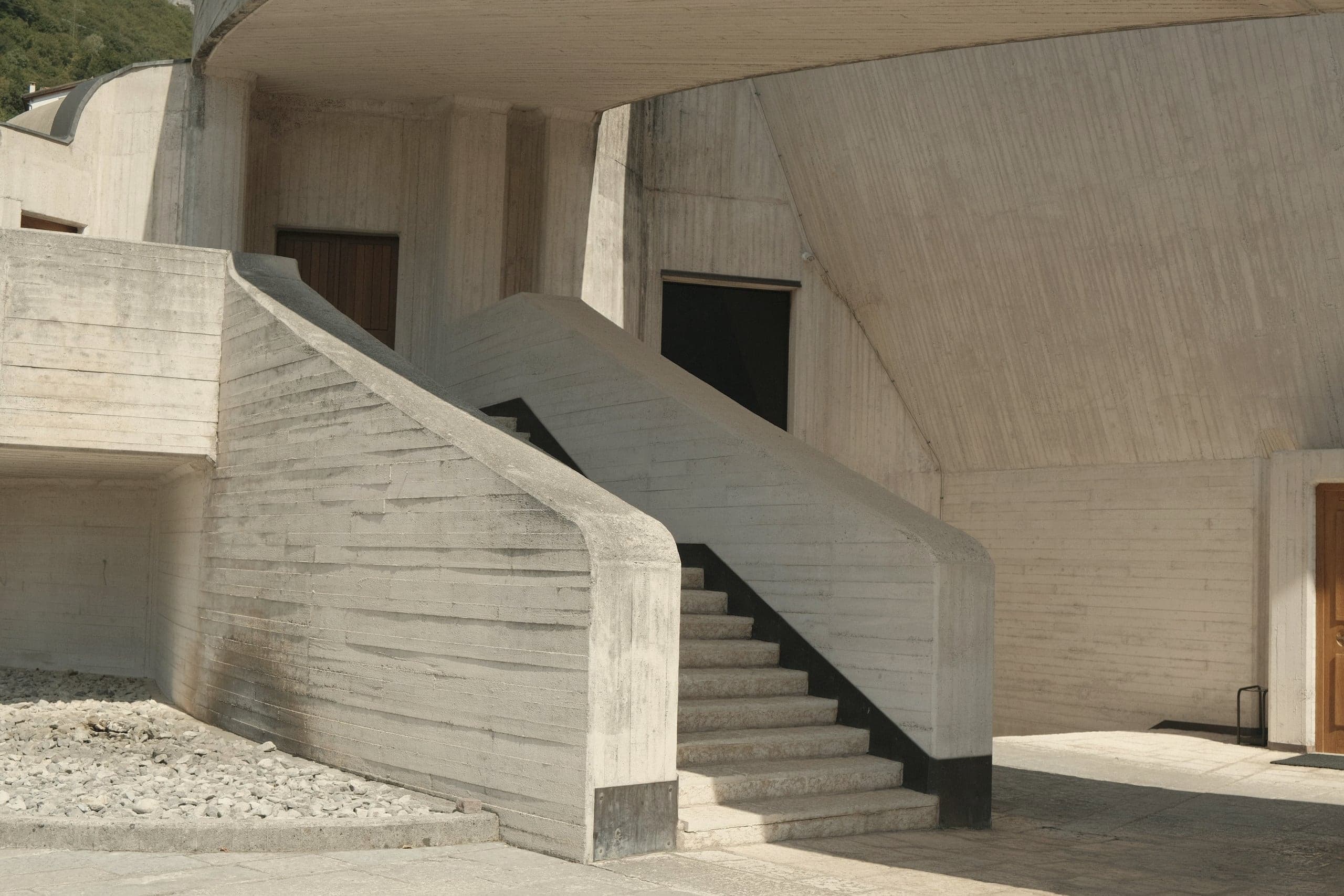A board-marked concrete stair curving beneath a deep overhanging roof.